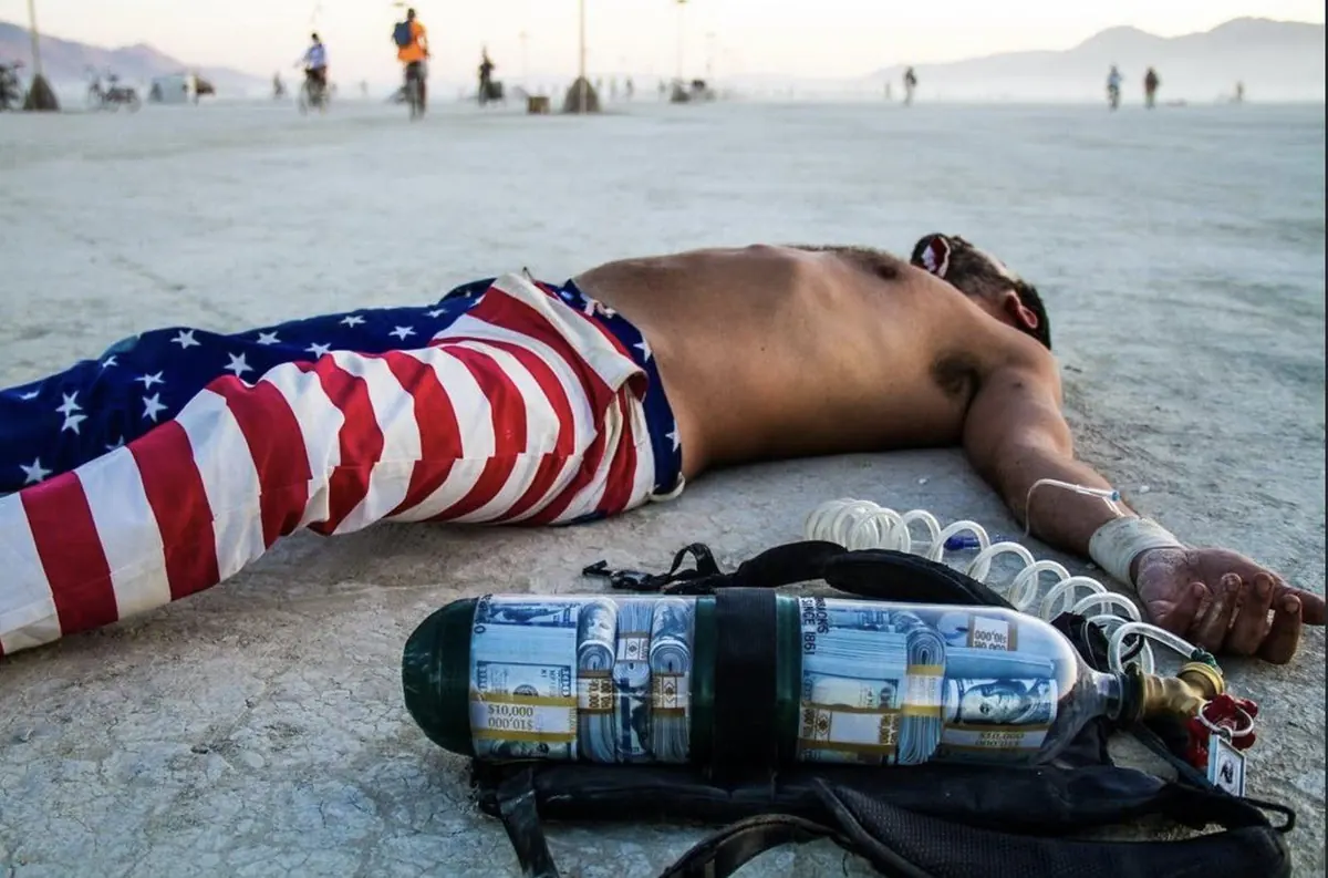 Capitalist Man — collapsed on the playa beside the money tank